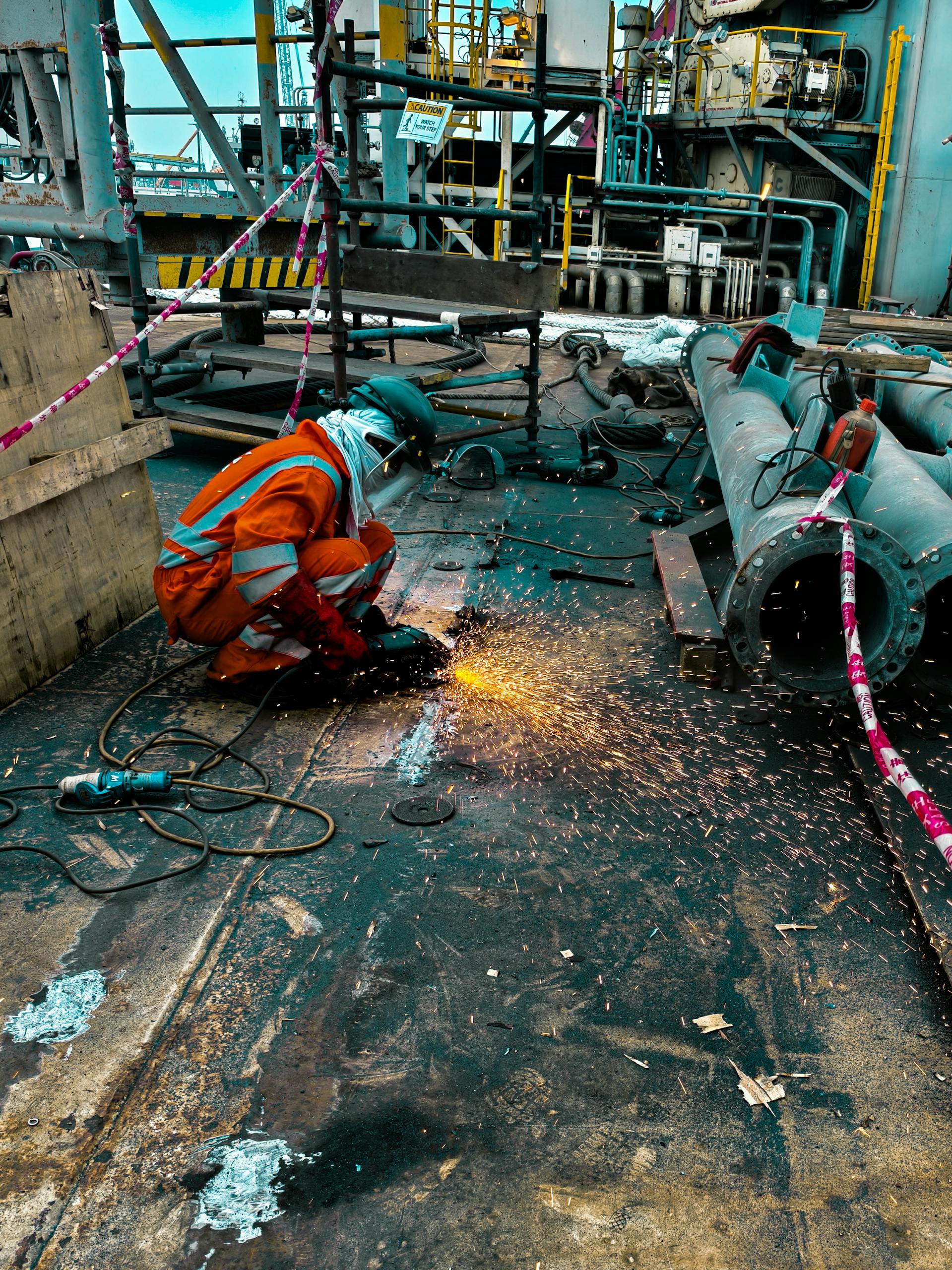A worker in safety gear welds metal on an offshore rig, with sparks flying.