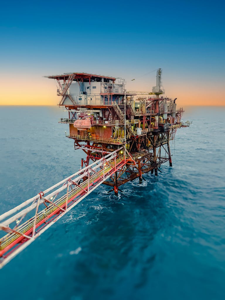 Aerial view of an offshore oil rig surrounded by the ocean at sunset, under a clear sky.